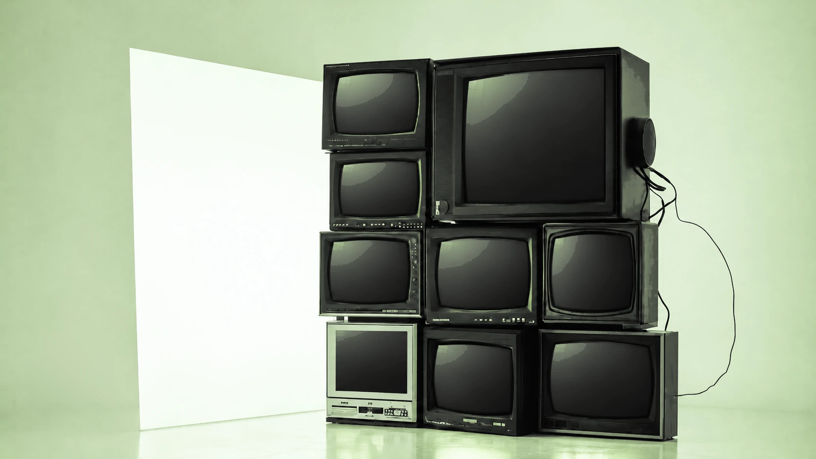 FRGG Open: a wall of nine old CRT televisions, all switched off, stacked beside a pale panel in a cool blue studio.